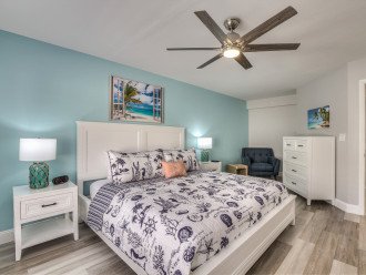 Angled photo of a bedroom displaying its nightstands, large bed, and ceiling fan.