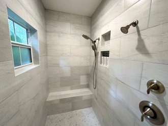 Spacious master walk-in shower with duo showerheads, handheld shower, and a bench