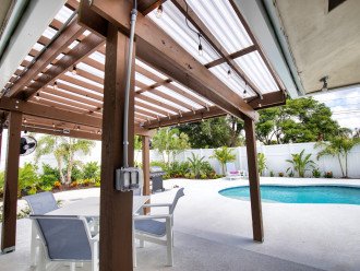 Patio area with covered pergola, dining table with four chairs, 65" TV and fan to keep you cool.