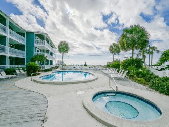 This picture shows the heated pool and hot tub located out the the patio gate of our beach condo. The pool is surrounded by a deck with lounge chairs, while the hot tub is tucked away in the corner. The crystal clear blue water sparkles in the sun, and th