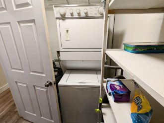 Laundry room with stacked washer and dryer. Door closes for quiet operation. Lots of shelf space wraps adjacent two walls.