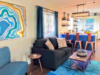 You'll enter the living room from the den. This communal space can seat up to 8 people = 3 on the copper chairs at the bar, 2 on the love seat, one in the turquoise accent chair and two on the two gray ottomans located under the TV console.