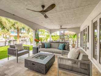 The covered patio contains a dining table for eight and a sitting area with TV and fire pit. The backyard turf holds an outdoor kitchen equipped with bar seating for six and a grill.