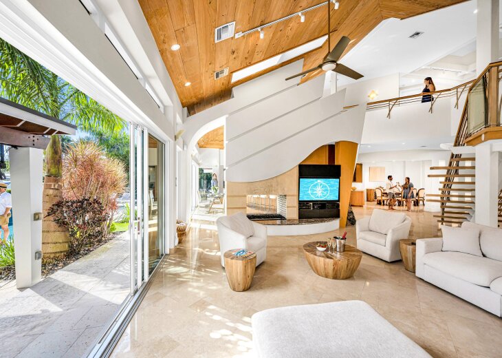 The extravagant living room includes a large smart TV, direct access to the covered outdoor entertainment area, and there is even a wet bar area beneath the open air staircase.