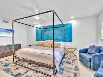 The master bedroom features a king-sized bed, wall-mounted flat screen Smart TV, and two comfortable chairs perfect for lounging.