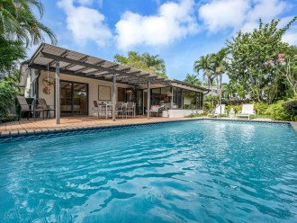 The backyard oasis is surrounded by lush tropical foliage with a heated pool, shaded patio and sunning area with loungers.