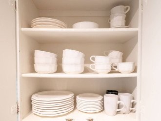 Kitchen cabinets include a variety of dishes, bowls and coffee cups