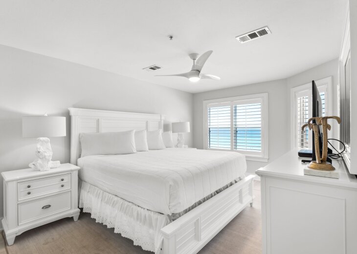 Drift off in this serene coastal bedroom with crisp linens, gentle sea breezes from the ceiling fan, and peaceful ocean glimpses through plantation shutters.