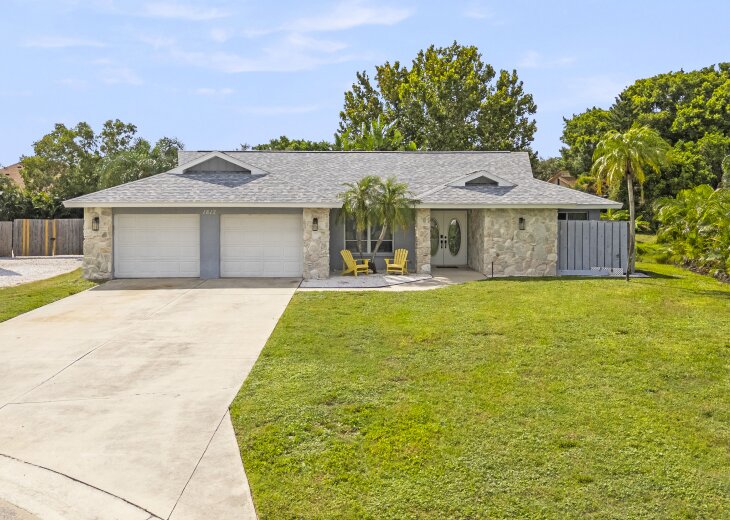 The property features a stone-accented facade with a welcoming covered entry and lush tropical landscaping, set in a quiet, established neighborhood.