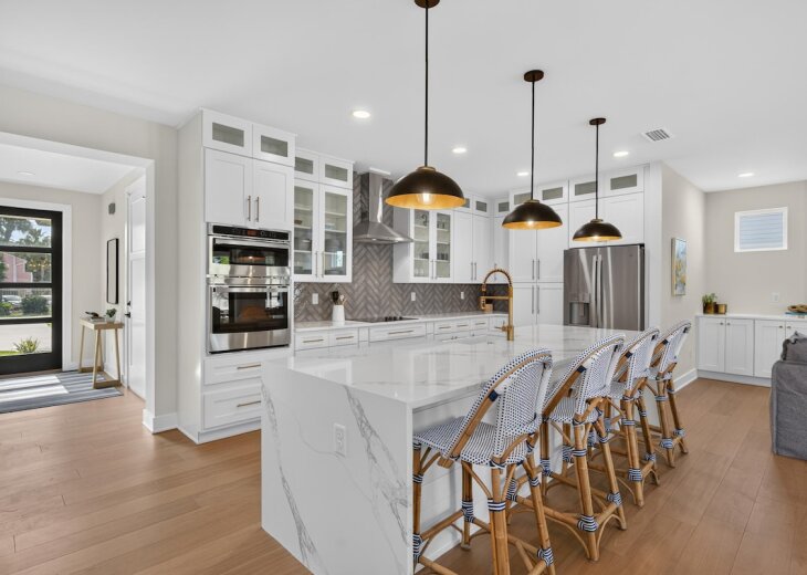 A chef's kitchen sports all the bells and whistles surrounded by glorious countertops, brass fixtures, white cabinetry, and a herringbone tile backsplash.