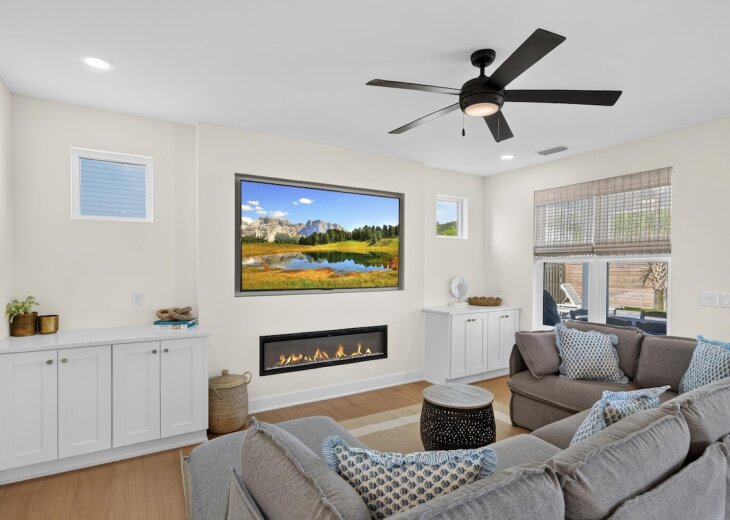 The living room features a wide gray sectional sofa and an 85" Smart TV above a cozy gas fireplace.
