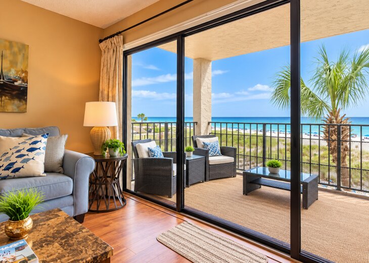 Cozy coastal living room with floor-to-ceiling sliding glass doors opening to a spacious, furnished balcony with beautiful Gulf views.