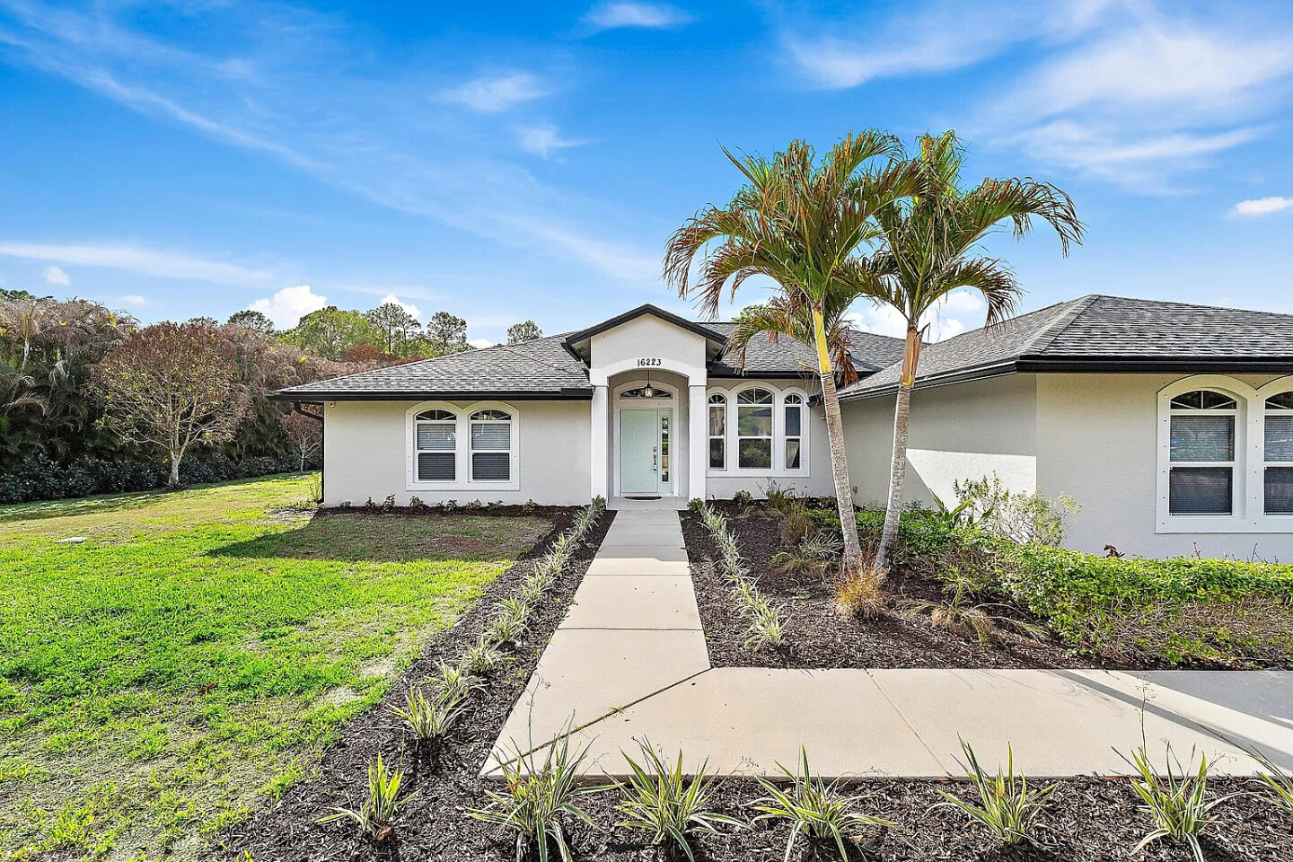 Front of the home: single-story with a palm-lined entry walk