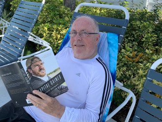Thomas O'Connor reading a book from the community library by the pool.
