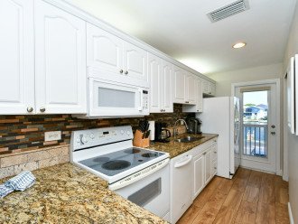 Modern, completely renovated kitchen with granite counter tops, glass tile back splash, opens to living/dining area and window/door overlooking the bay and boat docks
